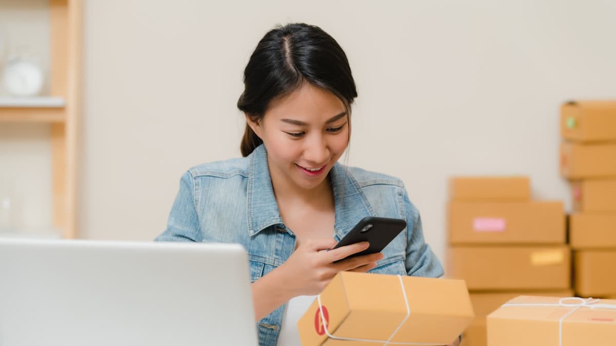 A seller checking an order on a phone beside packed parcels