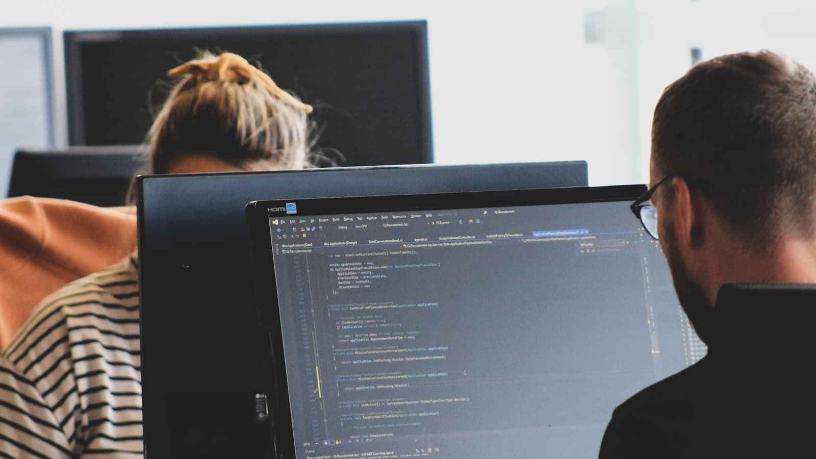 Two developers working through code on desktop monitors